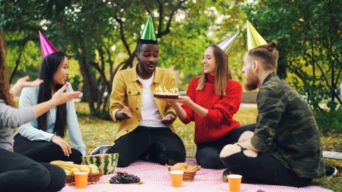 Friends celebrating birthday with cake at outdoor picnic.